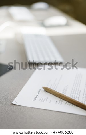 random syllabus with pen close up, with computers seen in the background. 