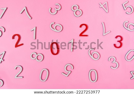 Random white numbers and red numbers 2,0,2 and 3 against pink background. Minimal creative concept for New Year 2023 season greetings card or banner or advertisement. No people. Flat lay