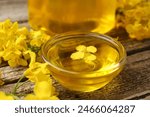 Rapeseed oil in glass bowl and beautiful yellow flowers on wooden table, closeup