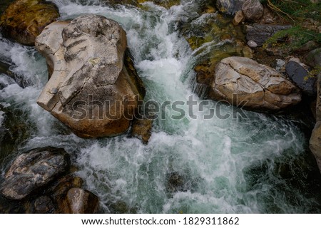 Rapid and powerful water flow between large rocks, close-up. Boulders in cold mountain river. Natural backgrounds.