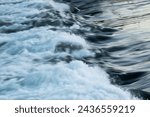 Rapid water flow over barrier with silky surface, river overflow over dam close up with splash and foam, abstract landscape pastel blue