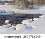 Rapids on the river at the end of winter: sunny day, stones in icy water, nature of Northern Europe, near Kerava in Finland.