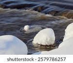 Rapids on the river at the end of winter: sunny day, stones in icy water, nature of Northern Europe, near Kerava in Finland.