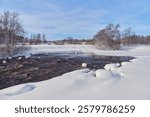 Rapids on the river at the end of winter: sunny day, stones in icy water, nature of Northern Europe, near Kerava in Finland.