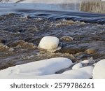 Rapids on the river at the end of winter: sunny day, stones in icy water, nature of Northern Europe, near Kerava in Finland.