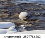 Rapids on the river at the end of winter: sunny day, stones in icy water, nature of Northern Europe, near Kerava in Finland.