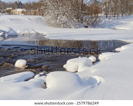 Rapids on the river at the end of winter: sunny day, stones in icy water, nature of Northern Europe, near Kerava in Finland.