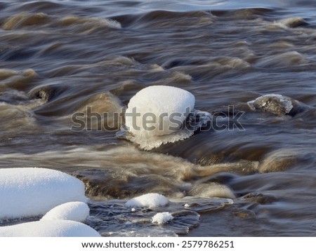 Rapids on the river at the end of winter: sunny day, stones in icy water, nature of Northern Europe, near Kerava in Finland.