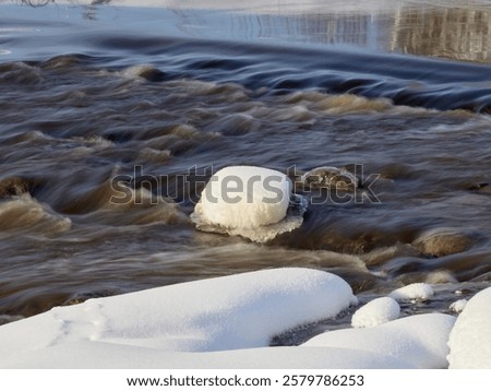 Rapids on the river at the end of winter: sunny day, stones in icy water, nature of Northern Europe, near Kerava in Finland.