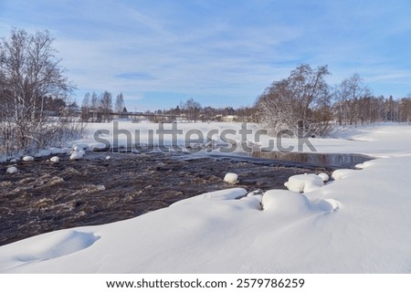 Rapids on the river at the end of winter: sunny day, stones in icy water, nature of Northern Europe, near Kerava in Finland.