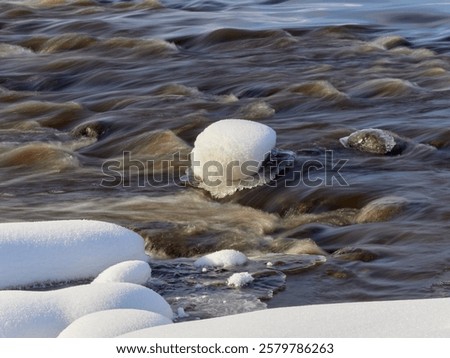 Rapids on the river at the end of winter: sunny day, stones in icy water, nature of Northern Europe, near Kerava in Finland.