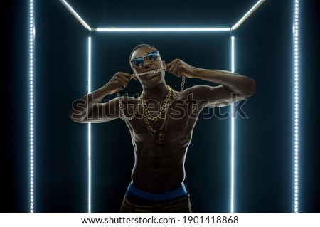Rapper in gold chains poses in illuminated cube
