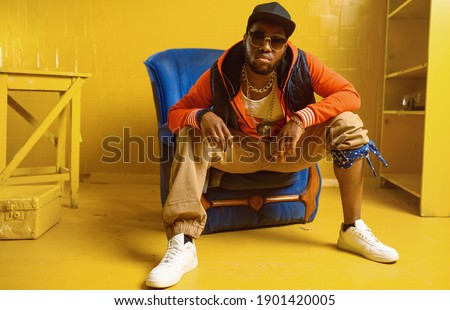 Rapper posing in chair in studio with yellow tones