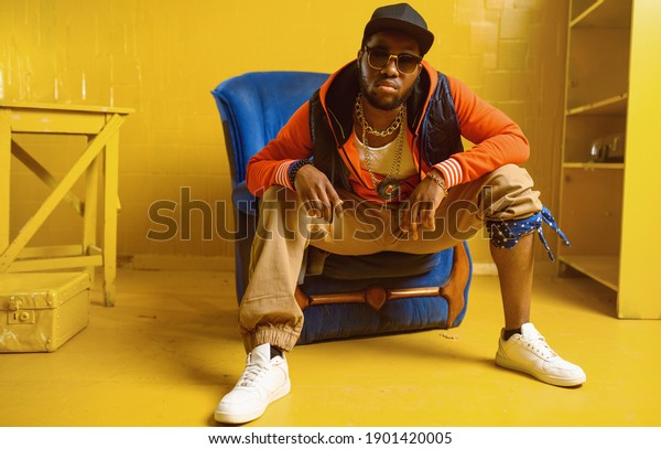 Rapper posing\
in chair in studio with yellow\
tones