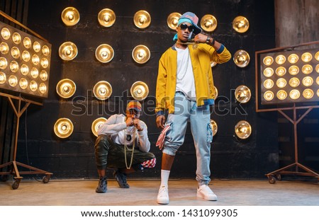 Rappers in caps dance on stage with spotlights