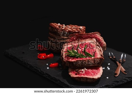 Rare cooking level Eye round steak with spices and herbs. Classic grilled meat cut ready to eat. Picnic or dinner concept. Hard light, dark shadow, black stone background, flat lay, close up