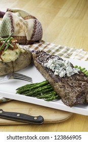 Rare New York Strip Steak On Asparagus Topped With Bleu Cheese With Bread And Twice Baked Potato