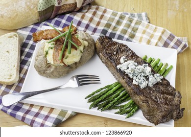 Rare New York Strip Steak On Asparagus Topped With Bleu Cheese With Bread And Twice Baked Potato