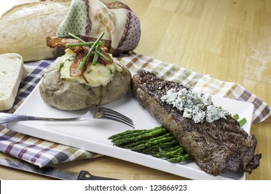 Rare New York Strip Steak On Asparagus Topped With Bleu Cheese With Bread And Twice Baked Potato