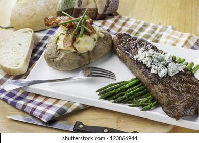 Rare New York Strip Steak On Asparagus Topped With Bleu Cheese With Bread And Twice Baked Potato