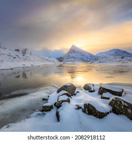 Rare northern snowy landscape in winter. The mountains are covered with snow. The texture of untouched snow in the foreground. The early morning sun tinted golden. Reflection in calm water. Winter 