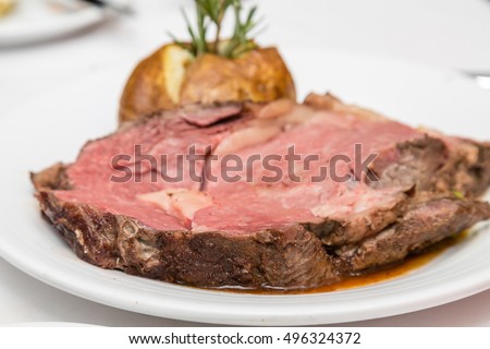 Rare prime rib of beef on a plate with baked potato and rosemary