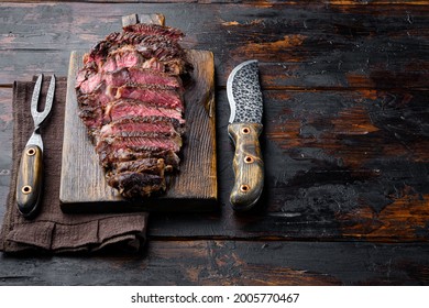 Rare rib eye steaks with herbs and spices set, on wooden serving board, with meat knife and fork, on old dark  wooden table background, with copy space for text
