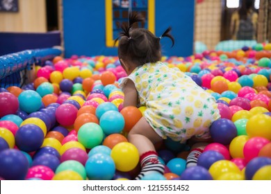 Rare Shot Of Little Girl Crawling And Having Fun In Ball Pit With Colorful Balls. Child Playing On Indoor Playground. Asian Kid In Ball Pool.