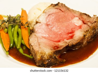 Rare Slab Of Prime Rib Beef On A Plate With Au Jus, Carrots, And Beans, Garnished With Rosemary