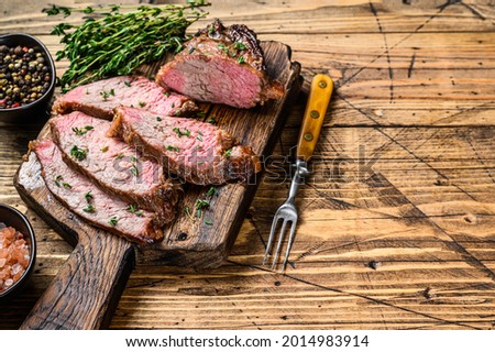 Rare slices of Roast beef sirloin tri tip steak bbq on a wooden cutting board. wooden background. Top view. Copy space
