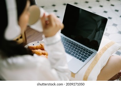 Rare View Of Beautiful Young Asian Woman Sitting Next To Her Bed Using Her Laptop And Enjoy Breakfast At Home. Small Business Owners Are Checking Orders Online. Concept For Freelancer Lifestyle.