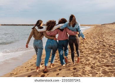 Rare view of  a four young women walking together barefoot on the beach - Powered by Shutterstock