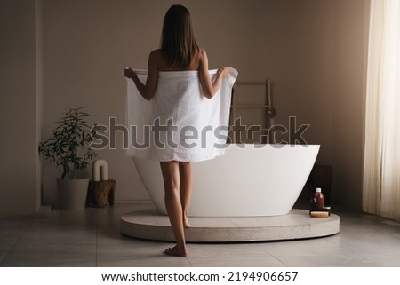Rare view full length portrait of girl taking towel off to take bath, to relax and rest, get clean and fresh standing in front of modern bathtub in stylish bathroom
