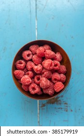 Rasberry In Brown Bowl On Blue Wooden Background.