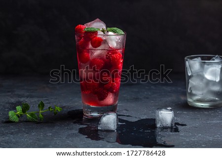 Raspberry alcoholic cocktail with liqueur, vodka, ice and mint on a dark background. Raspberry Mojito. Refreshing cool drink, lemonade or ice tea in a glass. Close up, copy space for text, low key