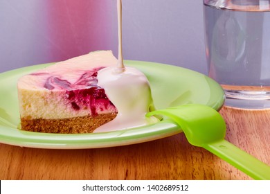 A Raspberry Cheese Cake Slice On A Green Plate With Thick Cream Being Poured On Top.