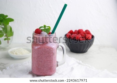 raspberry coconut smoothie with ice in a jar with straw, white background 