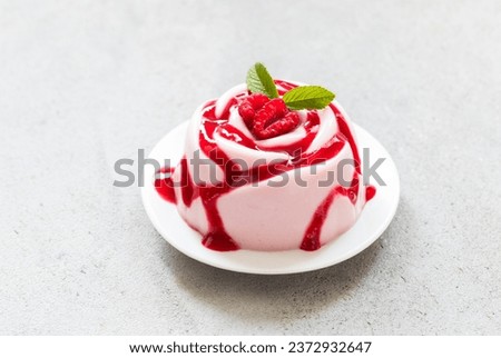 Raspberry cream dessert, Panna Cotta in the shape of a rose, with raspberry sauce, on a plate. Light grey background. Copy space
