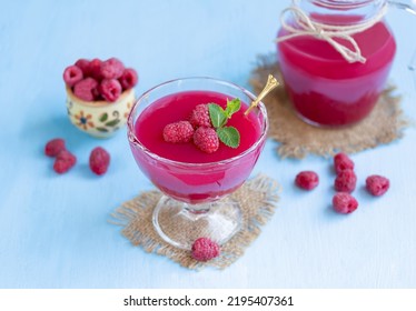Raspberry dessert in a glass. Traditional Russian thick berry drink or jelly dessert kissel made from fresh berries, water and corn starch. Glass of cold raspberry cocktail with fresh berries and jug 