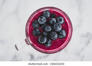 Raspberry And Dragonfruit Smoothie With Blueberries Topping In Pint Glass On Top Of White Marble Background