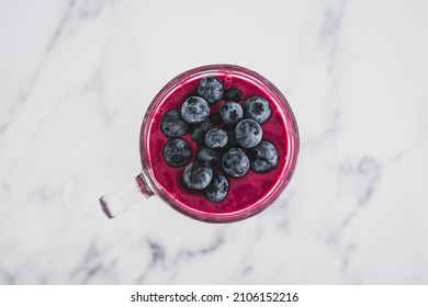 Raspberry And Dragonfruit Smoothie With Blueberries Topping In Pint Glass On Top Of White Marble Background