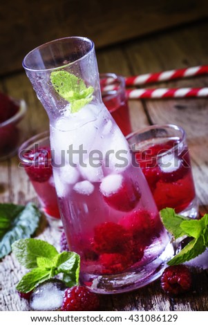 Raspberry drink with berries and ice in a glass pitcher on a dark wooden background, selective focus
