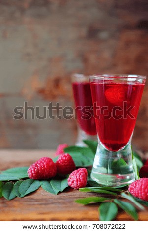 Raspberry fruit liqueur in two shot glasses with berries and green leaves. Strong local alcohol drinks.