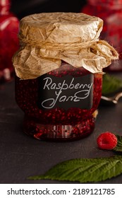 Raspberry Jam In Glass Jars, Ripe Raspberries On Dark Background. Organic Jam. Handwritten Label. Preserved Berries, Homemade Jam. 