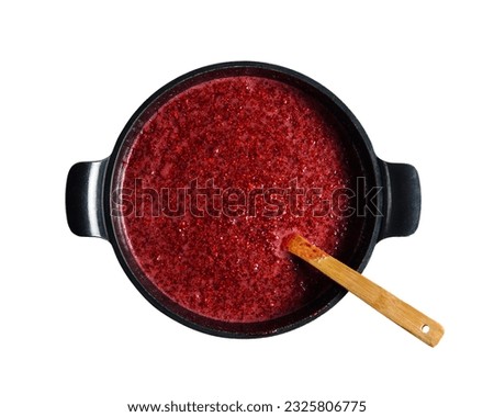 Raspberry jam in a large black saucepan. The wooden spatula lies inside. View from above. Isolated on a white background with a clipping mask. 