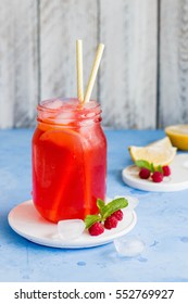 Raspberry Lemonade With Lemon, Lime, Mint And Ice In The Glass On The Blue Table Background. Summer Drink