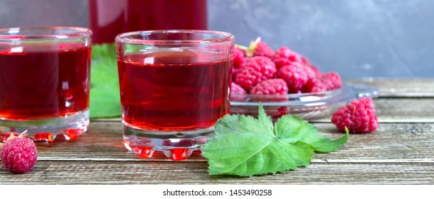 Raspberry liqueur in glass, fresh natural ripe organic berries and green leaves on a rustic wood background. Alcoholic flavored drink. Banner