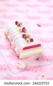 Raspberry Lychee and Rose Yule Log Cake covered with pink glaze and decorated with rose meringue cookies, on a light pink background.