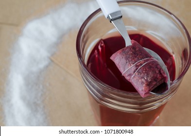 Raspberry Tea In Glass And Tea Bag On White Spoon, Spilled Sugar Around, On Light Retro Background