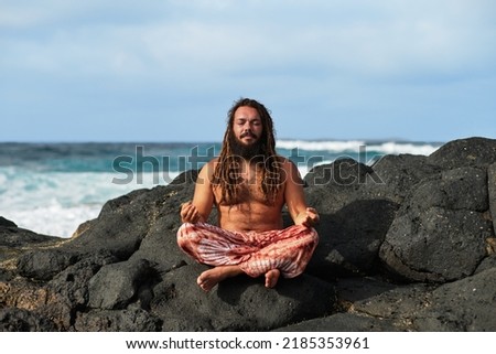 rasta boy meditating in lotus position, by the sea